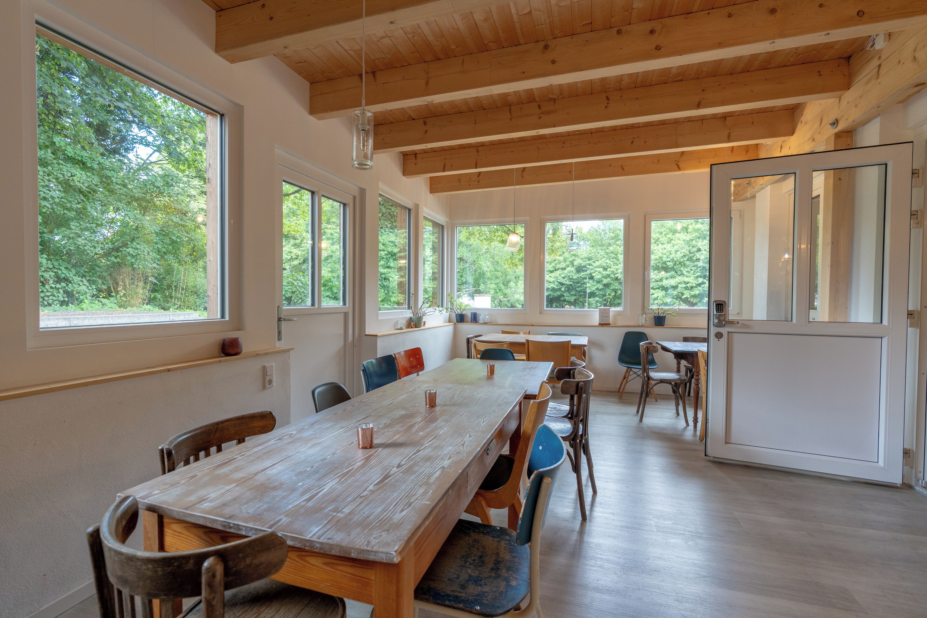 Un comedor amplio con una larga mesa de madera, varias sillas y ventanas grandes que dan vistas a zonas verdes.