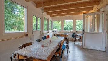 Un comedor amplio con una larga mesa de madera, varias sillas y ventanas grandes que dan vistas a zonas verdes.