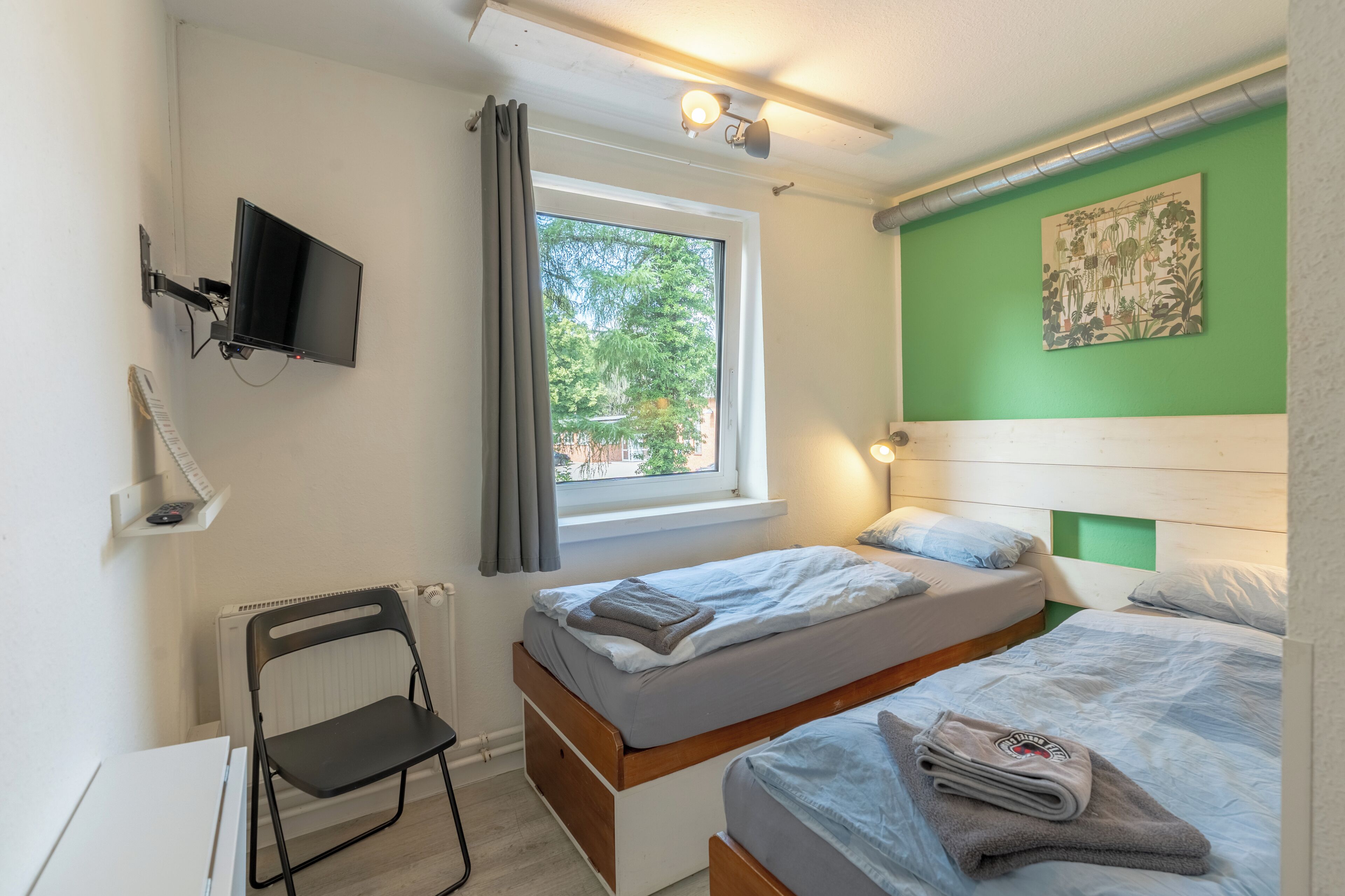 A room with two beds, a desk, a chair, a TV, and a window with curtains.