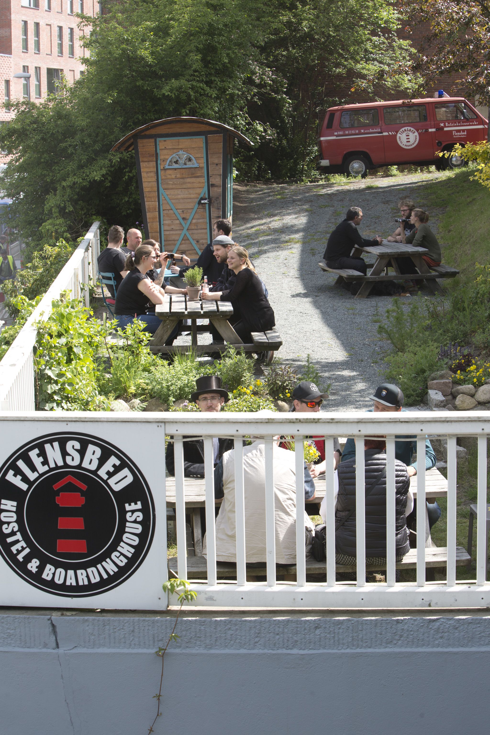 A hostel with outdoor seating and a red van in the background.