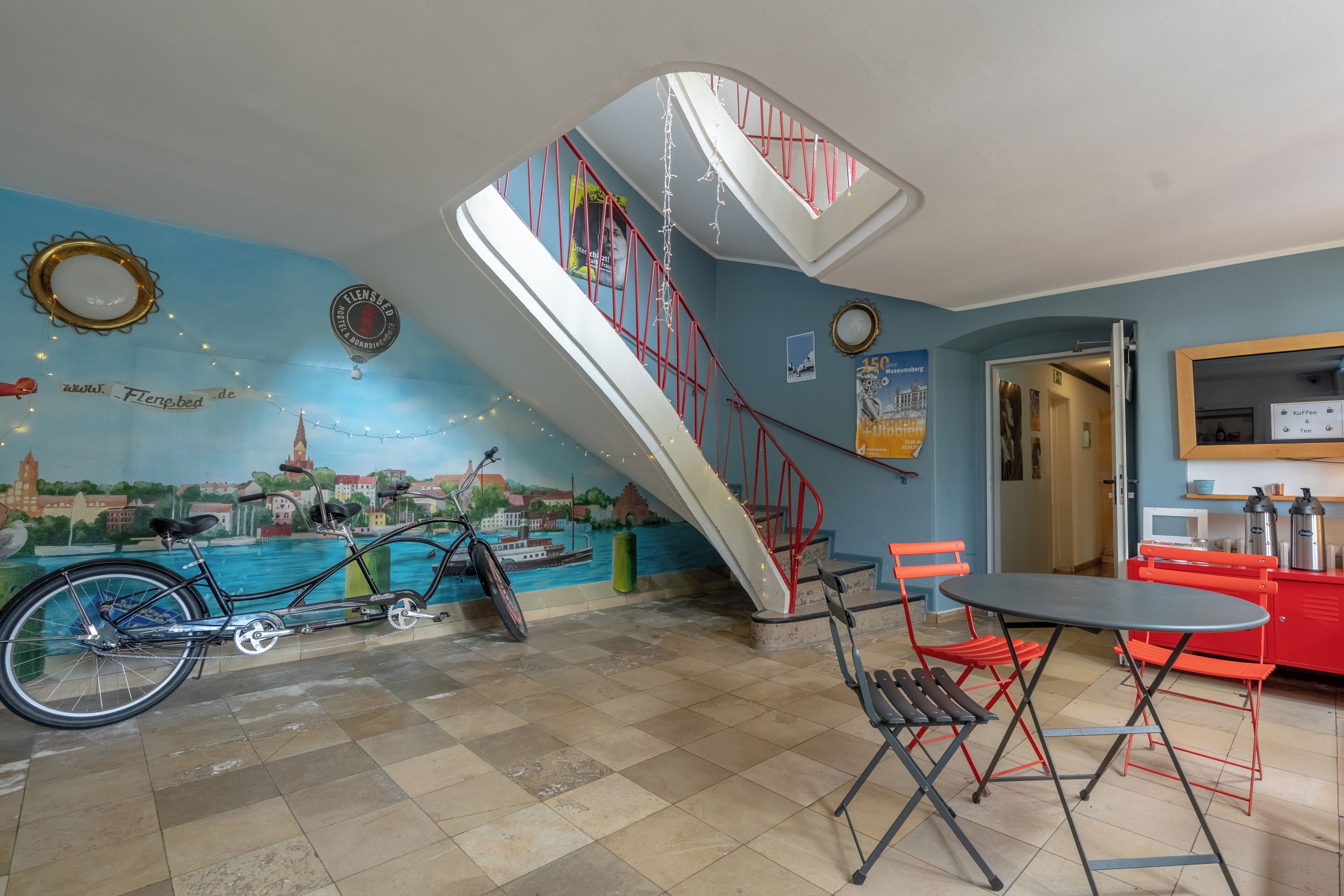 A room with a bicycle, a table, chairs, a staircase, and a mural.