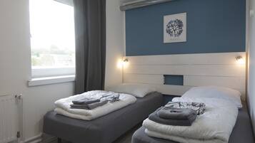 Una habitación con dos camas, una ventana con cortinas, un radiador y una lámpara fijada a la pared.