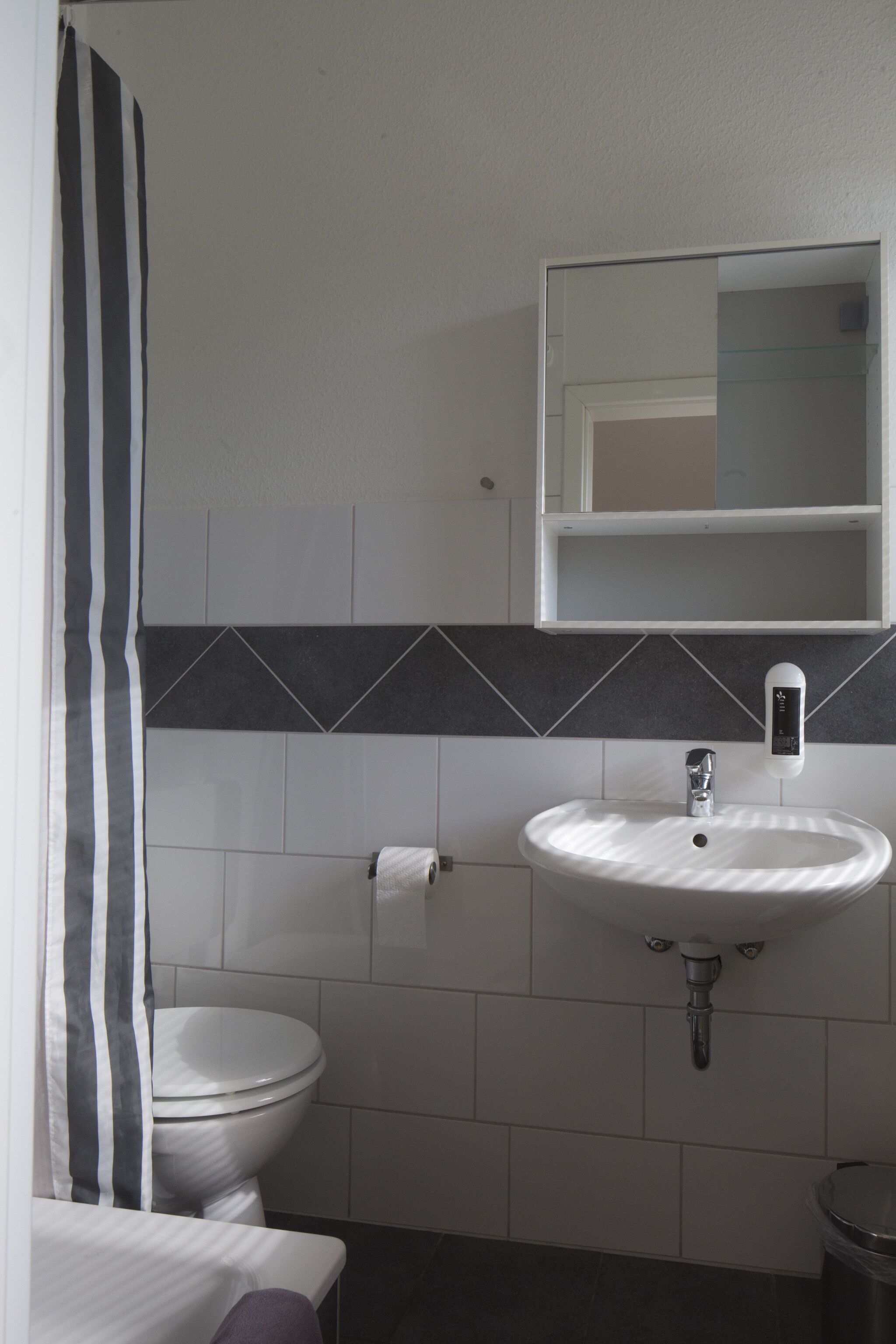 Un baño con lavamanos blanco, inodoro y espejo sobre el lavamanos.