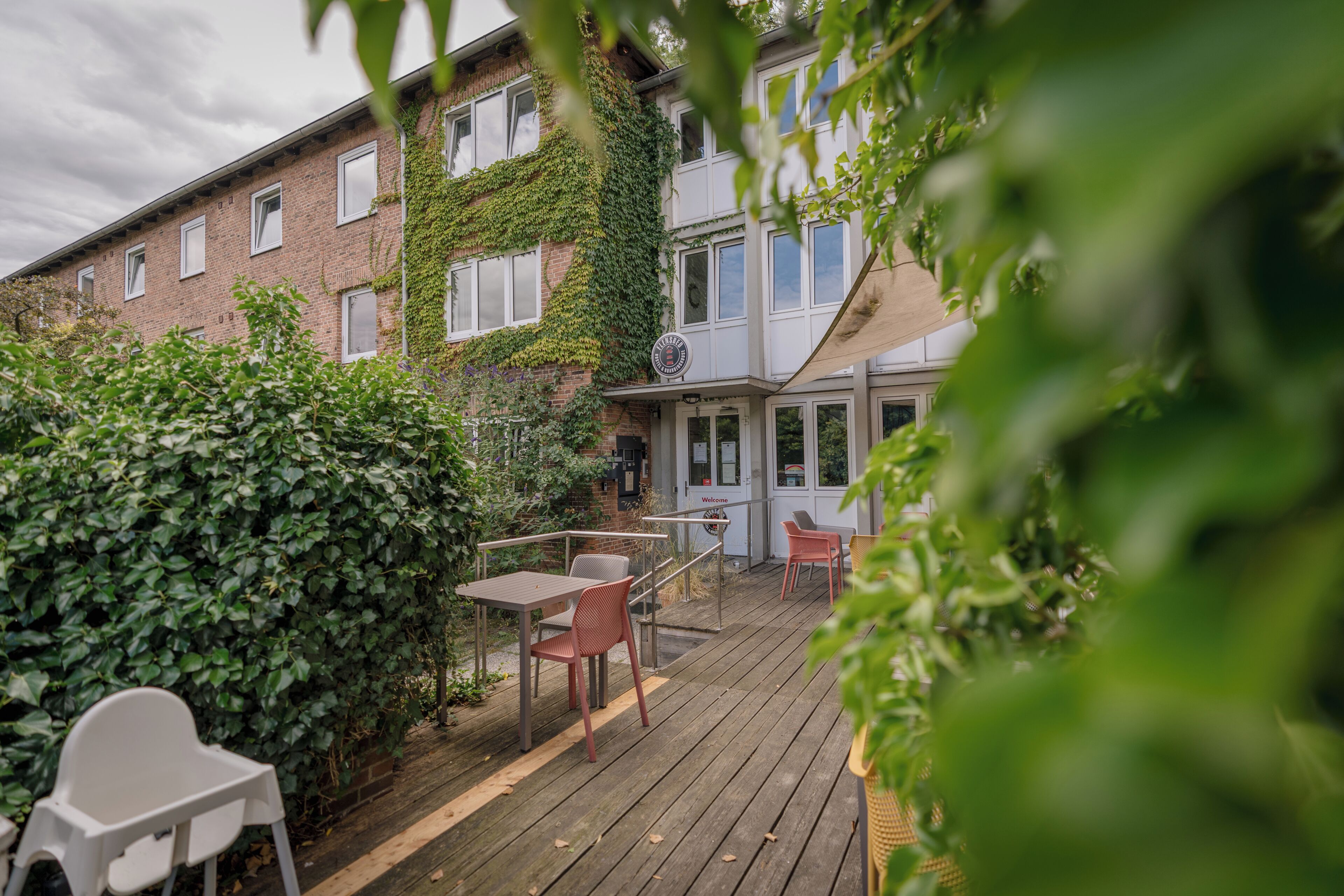 Eine Holzterrasse mit Sitzgelegenheiten im Freien, ein mit Efeu bewachsenes Backsteingebäude und ein Schild, das ein Restaurant anzeigt.