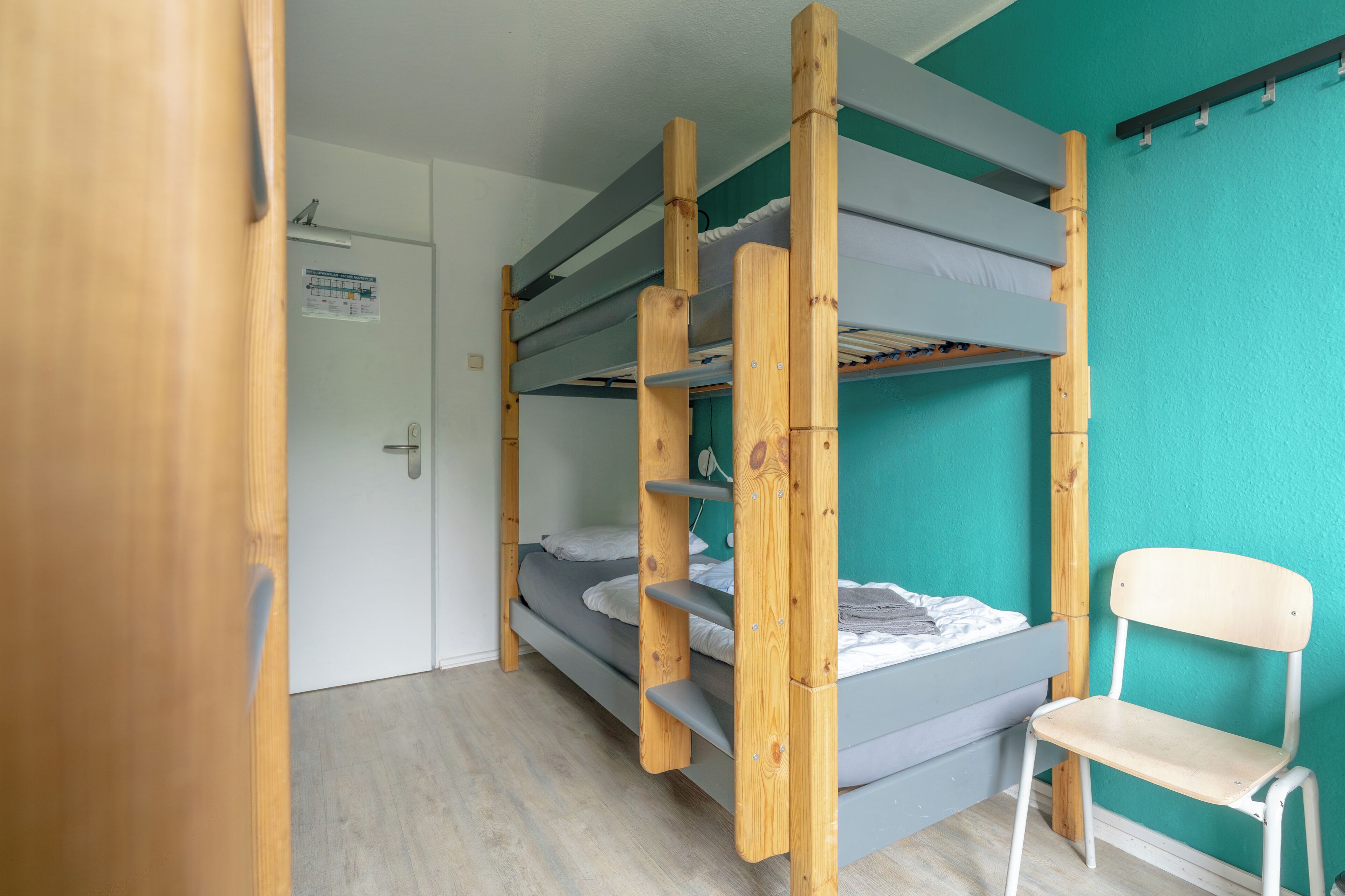 Habitación con literas, una escalera de madera, una silla blanca y pared color aguamarina.