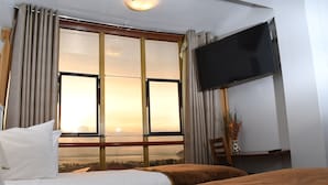 Habitación de hotel con dos camas, televisión, ventana con cortinas y vista a la ciudad.