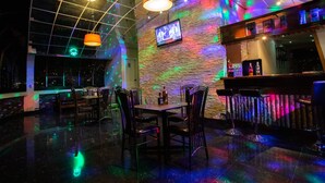 Zona de bar con pared de piedra, varias lámparas colgantes y una barra con botellas.
