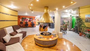 Un hall con una mesa redonda de madera rodeada de libros, una chimenea grande de color dorado y una zona de estar con sofás.