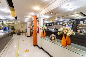 Zona de recepción de hotel con un mostrador de vidrio, jarrones anaranjados con flores y un cartel que indica una zona para fumadores.
