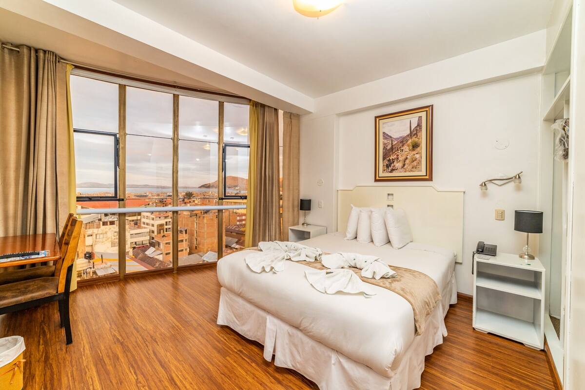 Ein Hotelzimmer mit großem Fenster, einem Bett, einem Schreibtisch und einem Stuhl.