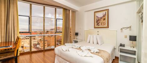A hotel room with a large window, a bed, a desk, and a chair.