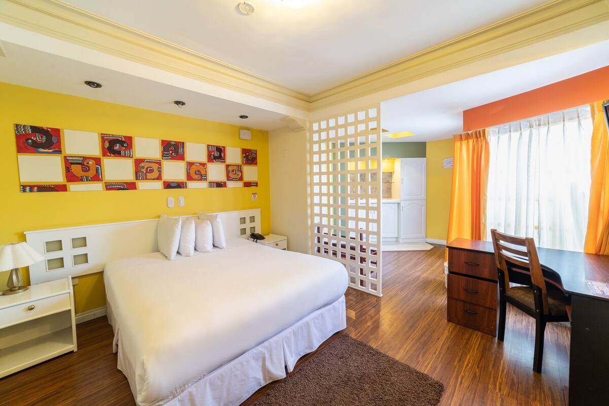 Ein Hotelzimmer mit Bett, Schreibtisch und Stuhl. Eine Trennwand mit Gittermuster und ein Fenster mit Vorhängen.