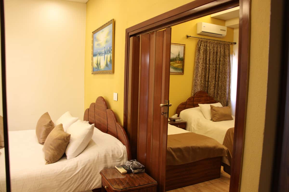 Habitación de hotel con dos camas, cabeceros de madera, una mesita de noche de madera y un cuadro en la pared.