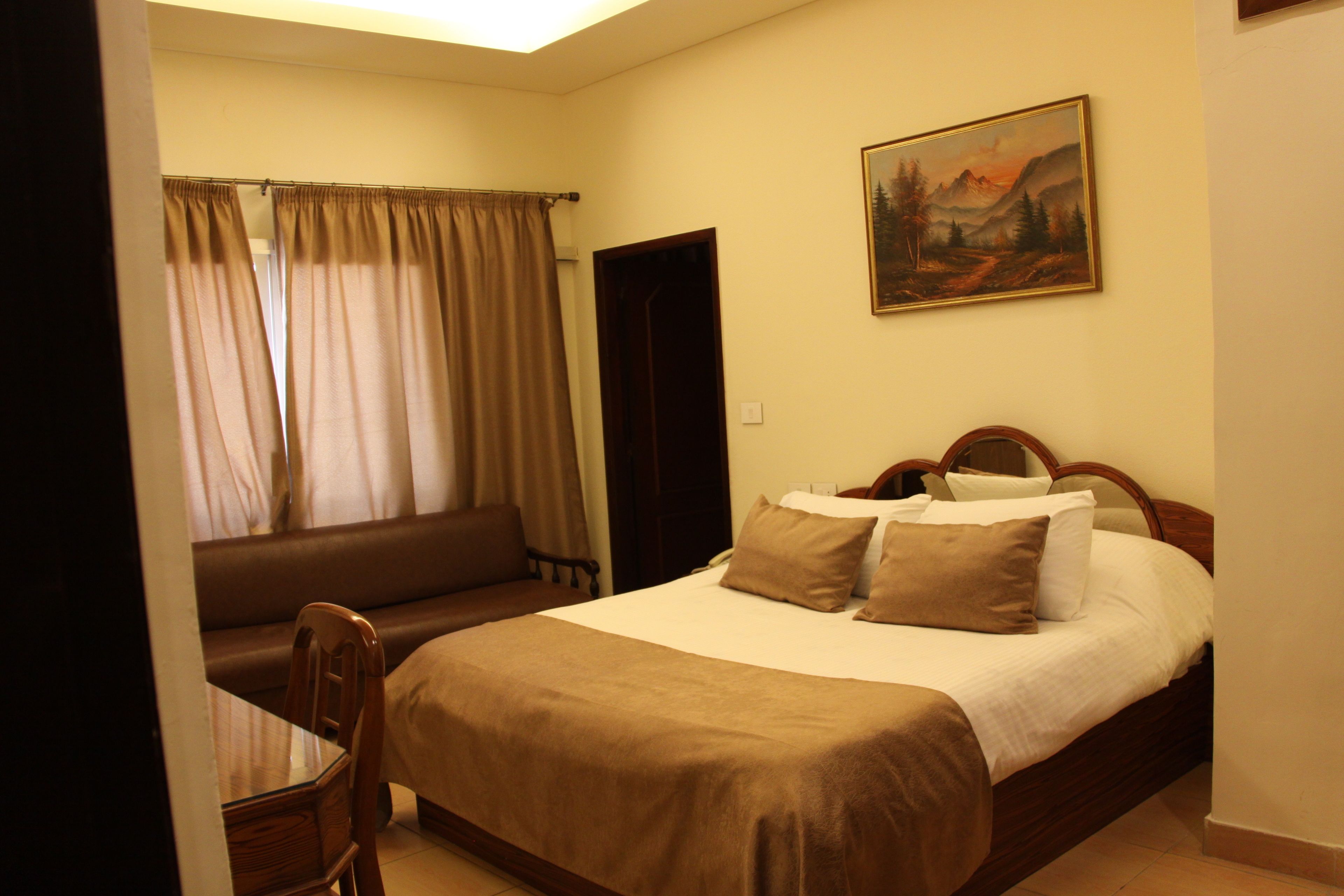 A bedroom with a bed, a chair, a painting on the wall, and a window with curtains.