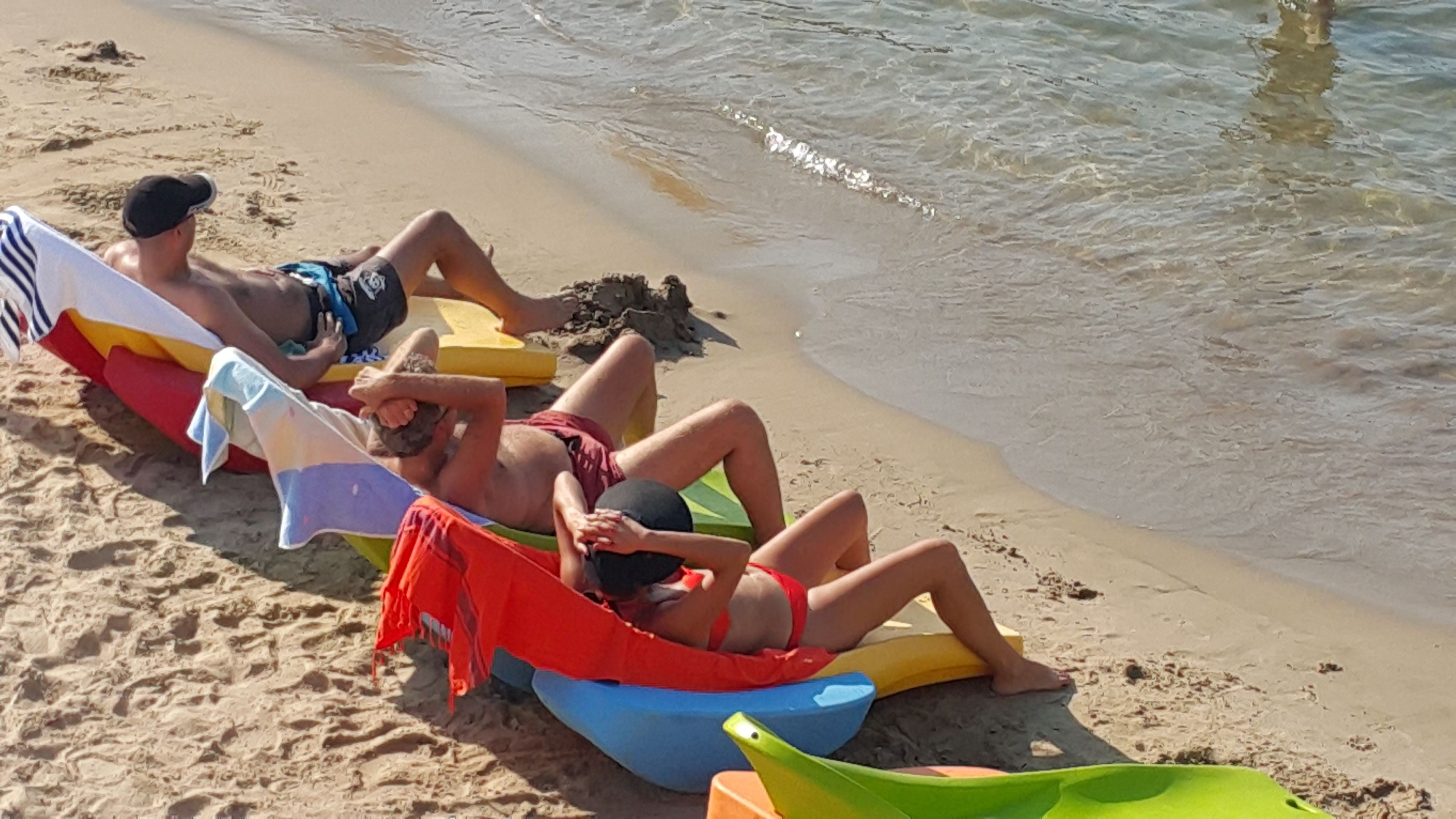 Escena de playa con gente descansando en sillas de playa coloridas y una hamaca.