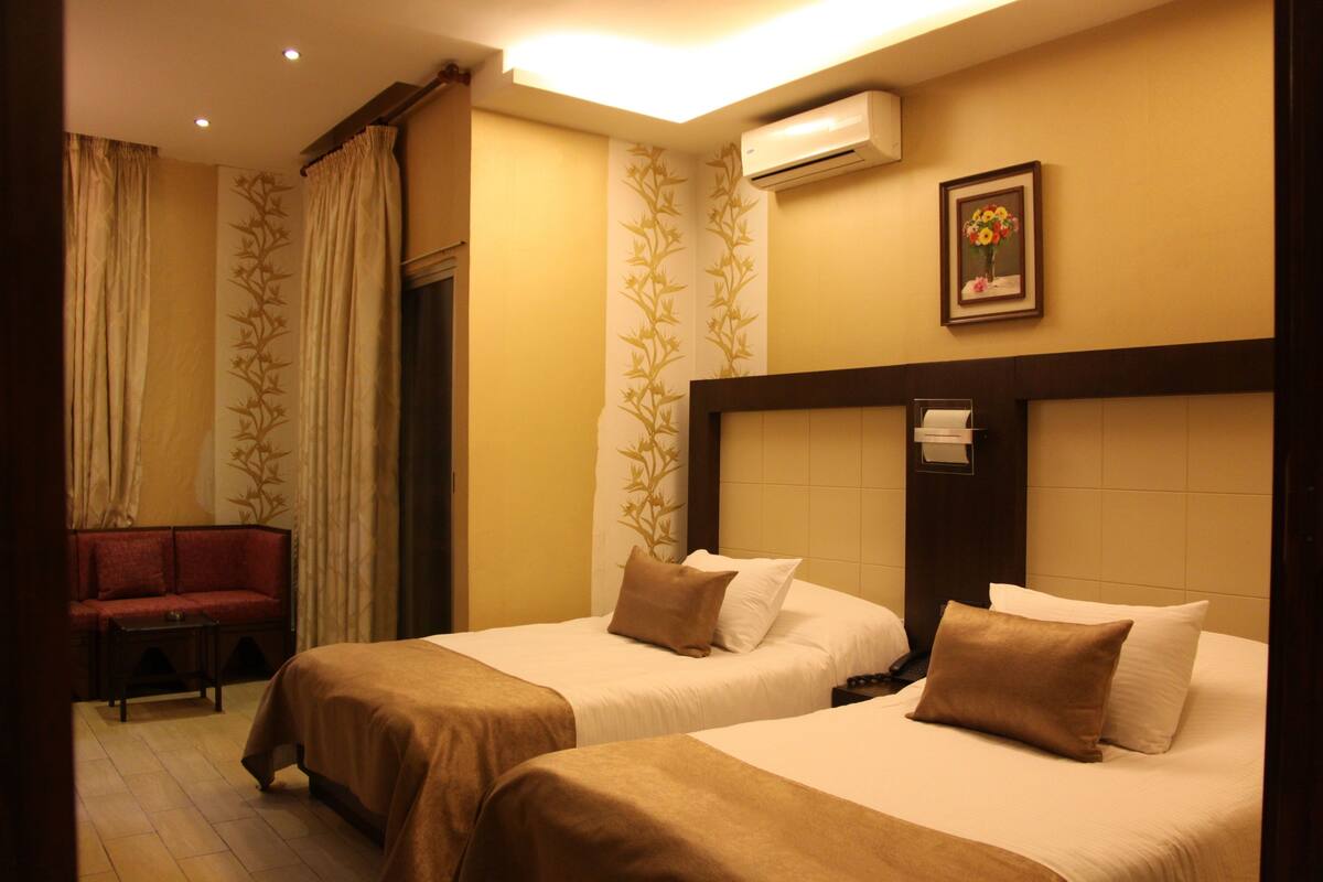 Habitación de hotel con dos camas, un sofá y un equipo de aire acondicionado.