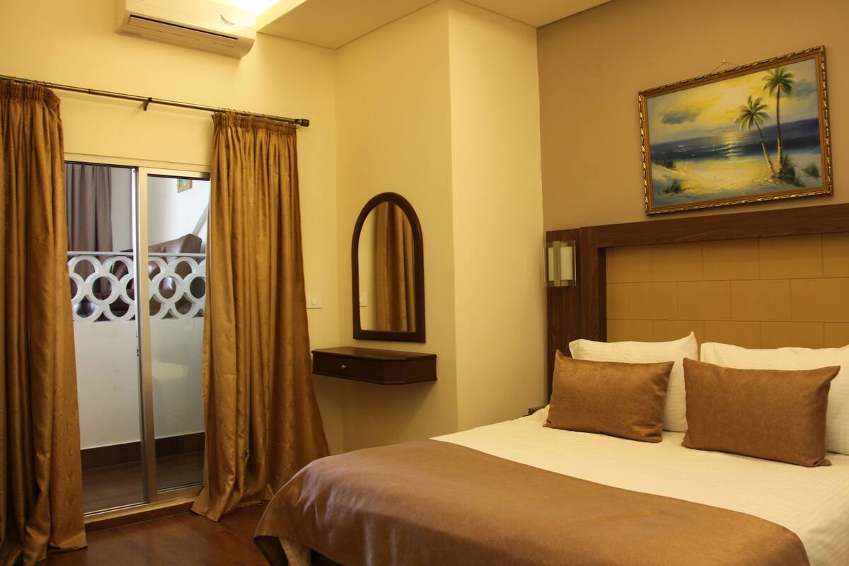 Habitación de hotel con cama, un cuadro de una playa, un espejo y una puerta corrediza con cortinas.