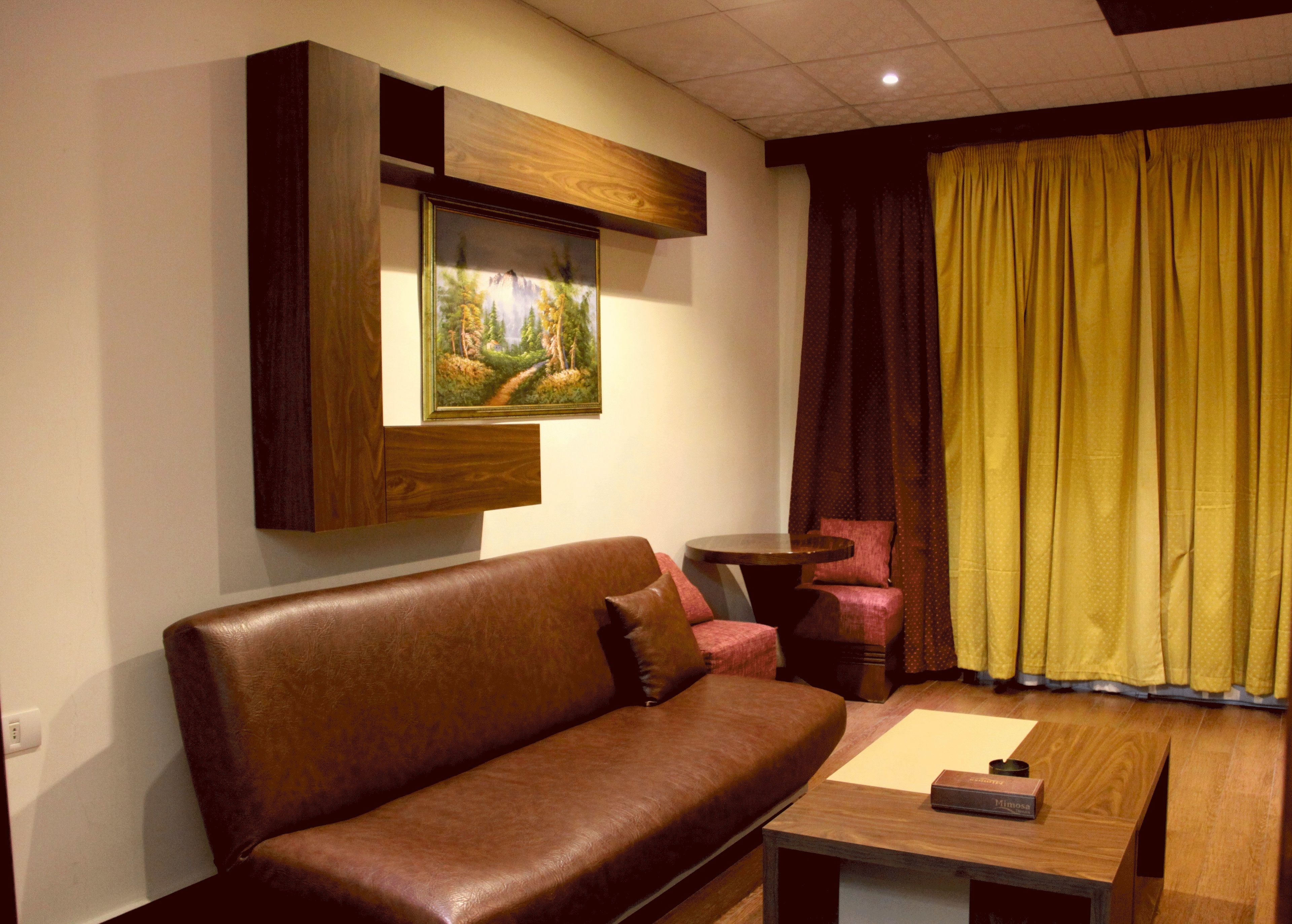 A living room with a brown leather sofa, a small round table, and a painting on the wall.
