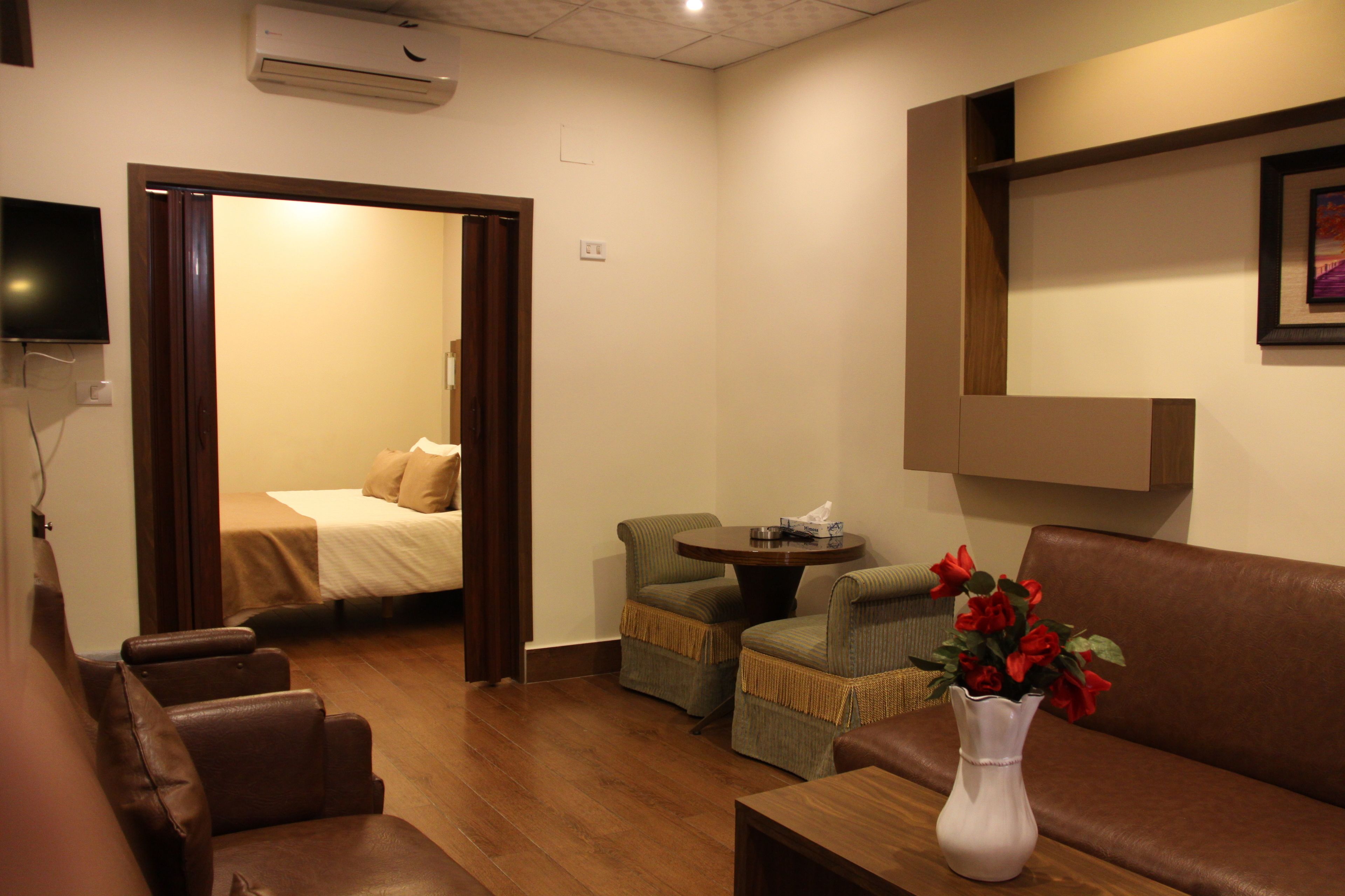 Habitación de hotel con cama, zona de estar con sofá y sillones, una mesita y un jarrón con flores.