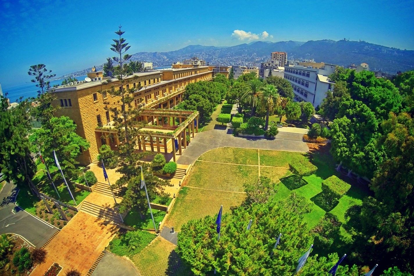 A courtyard with a building, trees, and a view of the sea.