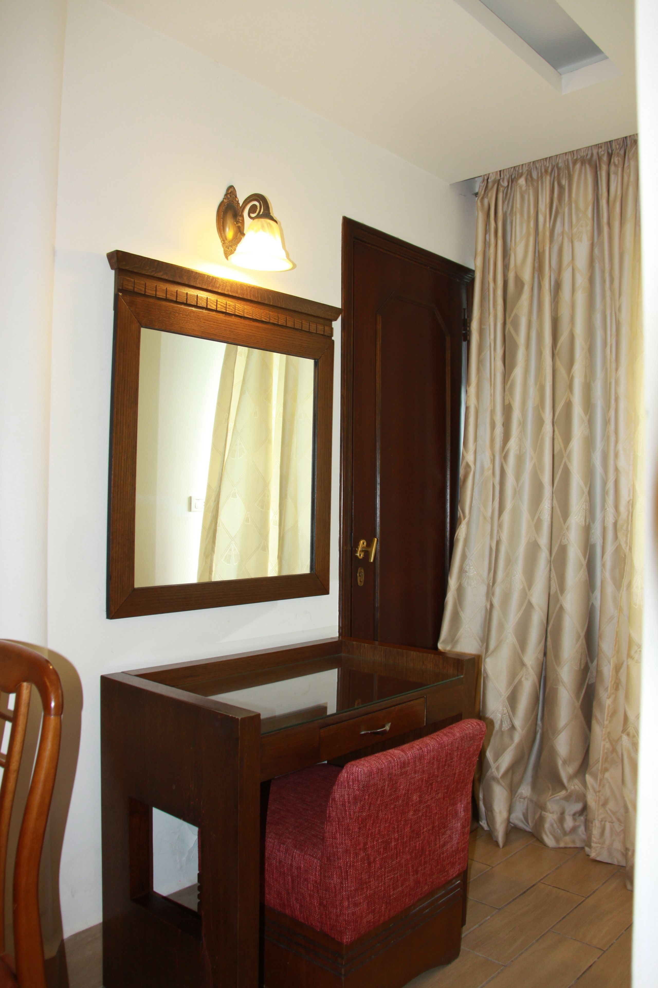 Una habitación con un aparador de madera, un espejo, una silla roja, una puerta de madera y una cortina.