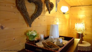 Een houten interieur met een krans in de vorm van een hart, een wandlamp en een tafel met een dienblad waarop een kaars, glaasjes en een kleine plant staan.