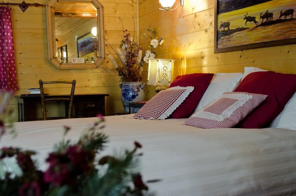Ein Zimmer aus Holz mit einem Bett, einem Spiegel, einer Vase mit Blumen und einem Bild an der Wand.