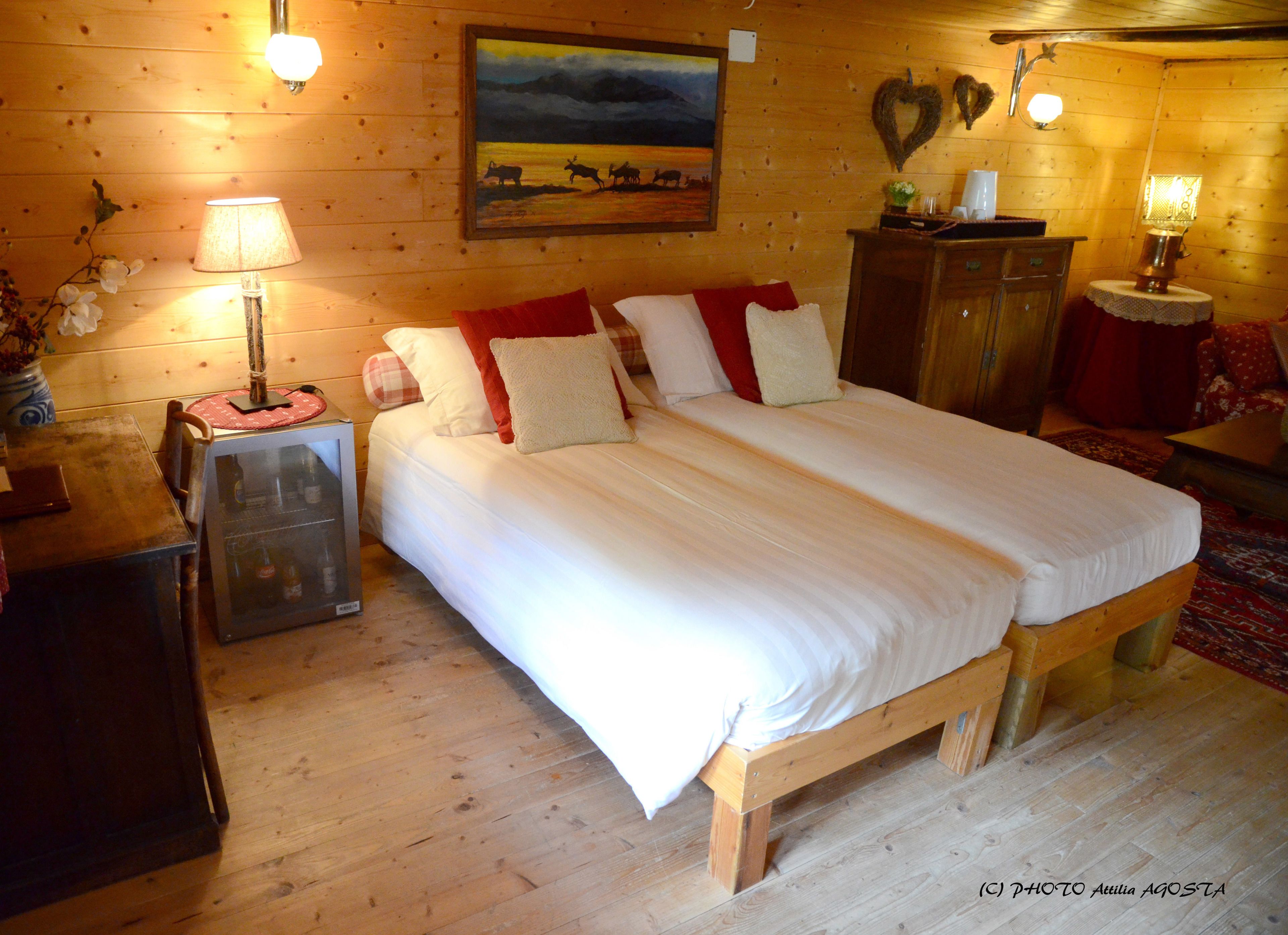 A wooden room with a bed, two bedside tables, a dresser, and a painting on the wall.