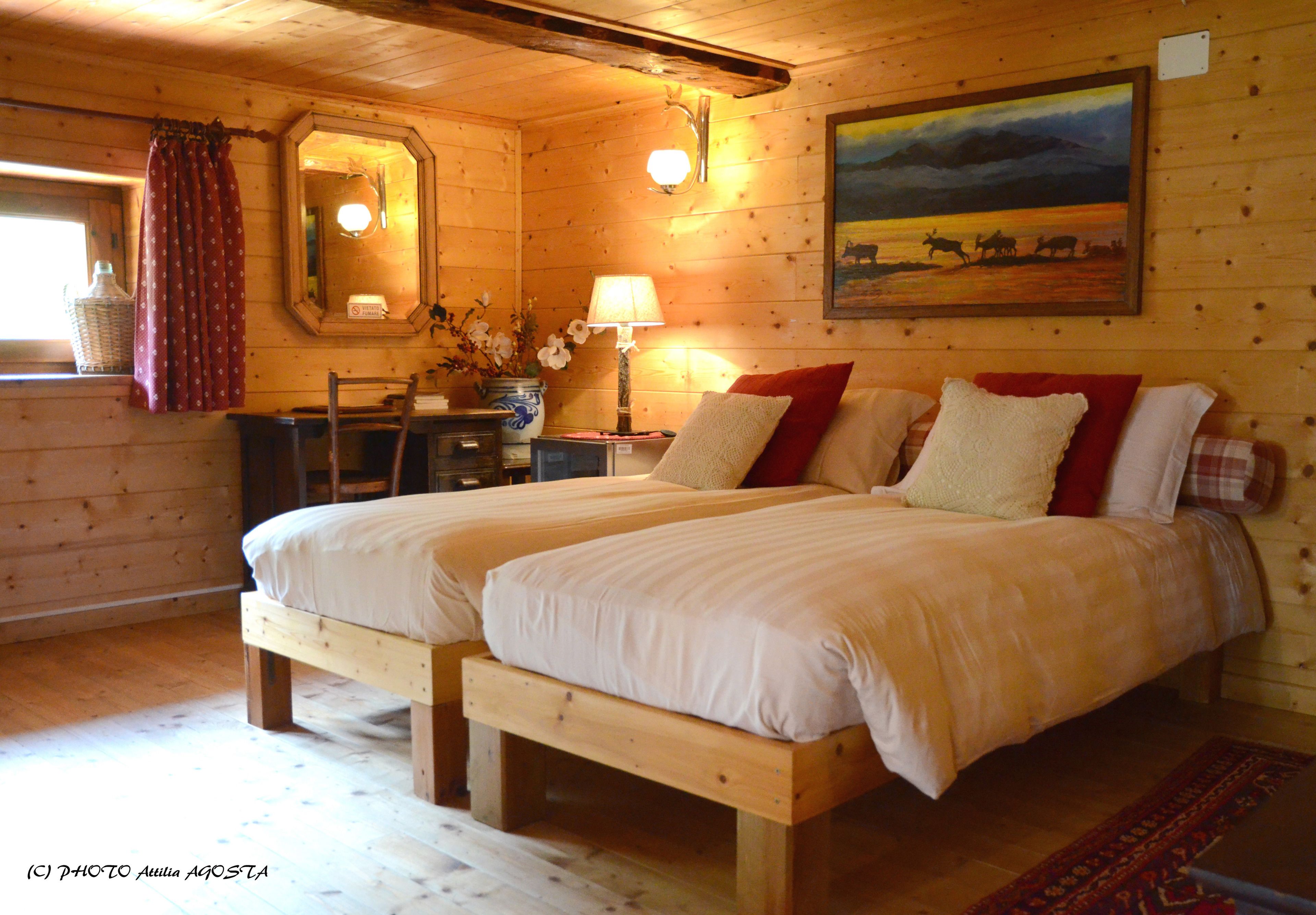 A wooden cabin bedroom with two beds, a dresser, a mirror, and a painting on the wall.