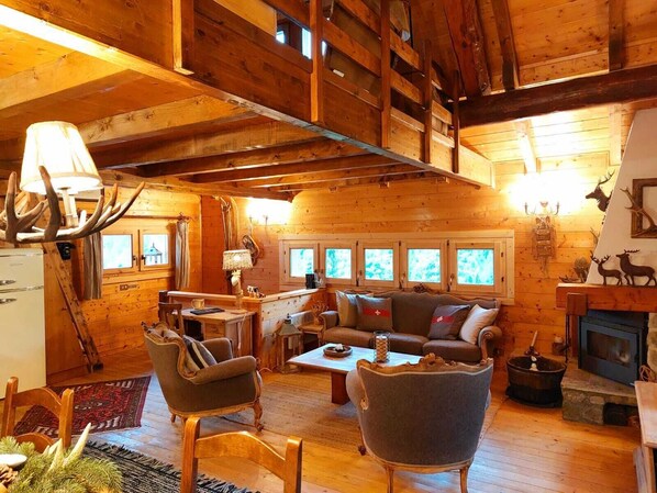 A cozy log cabin interior with a wooden ceiling, a sofa, chairs, a fireplace, and a dining area. - CHALET DEI FIORI - ROOM & APARTMENT (Bedretto)