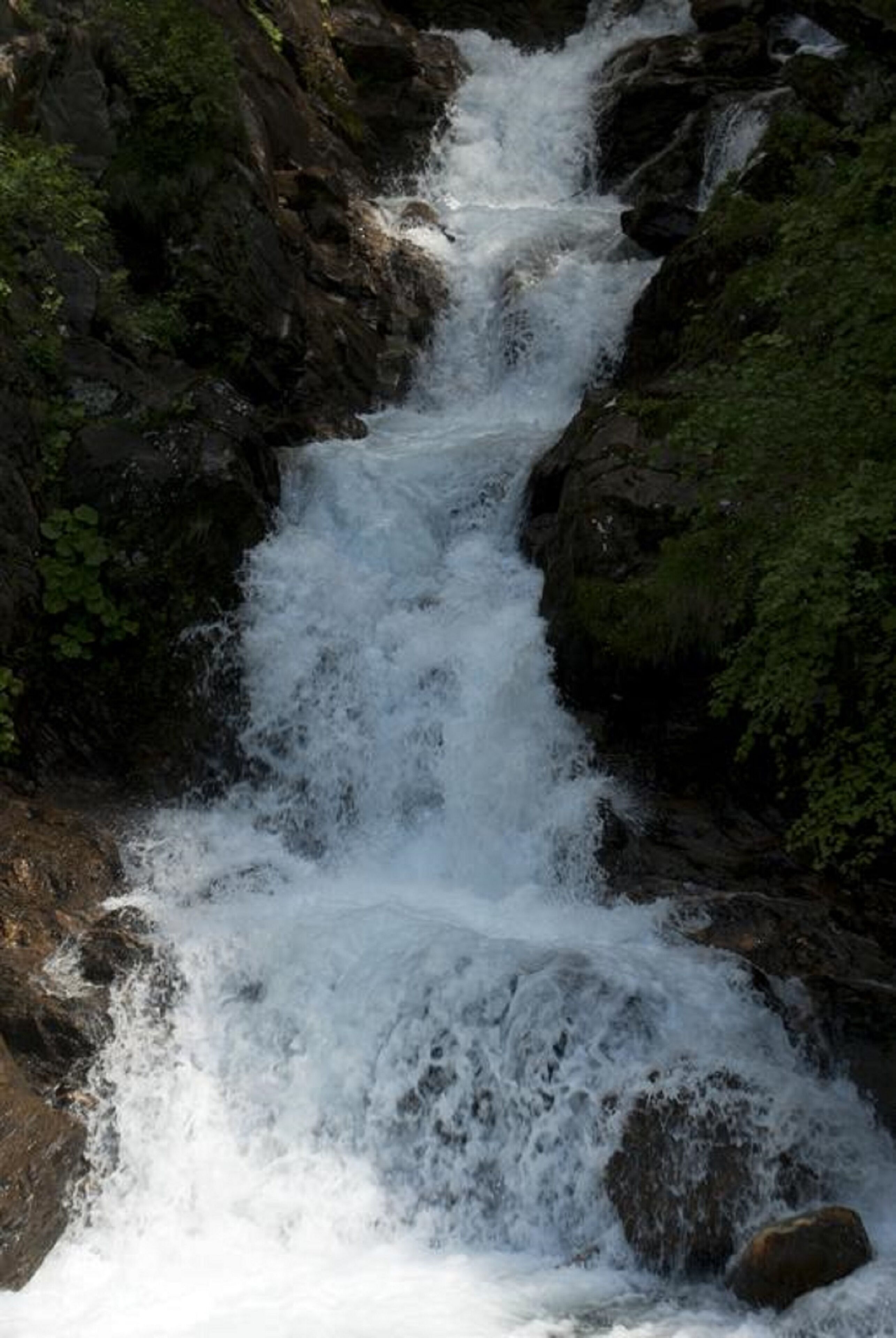 A waterfall cascading over dark rocks with lush greenery around.