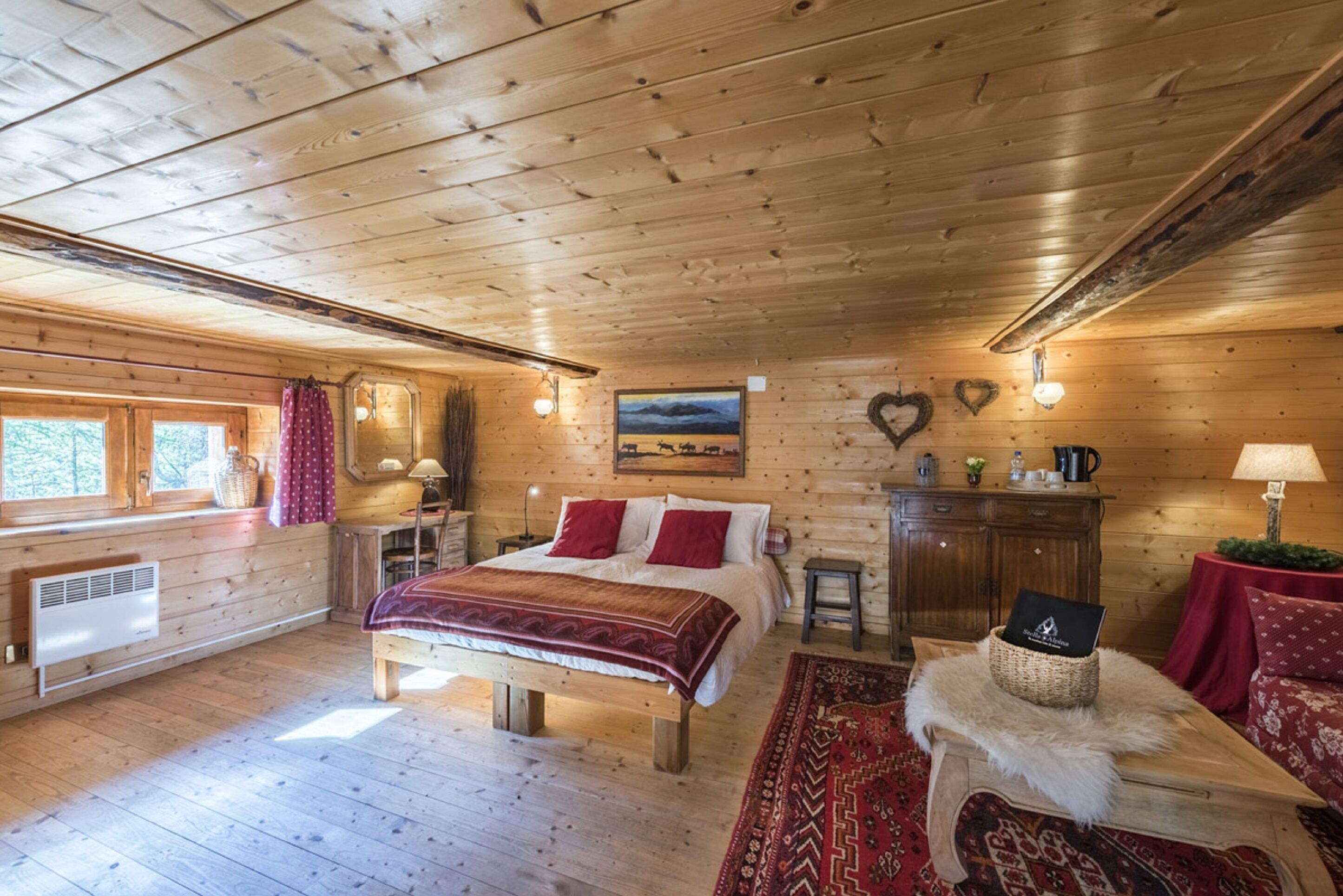 A wooden cabin bedroom with a bed, dresser, and a window with curtains.