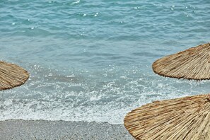 A beach scene with thatched umbrellas and the ocean waves. - Atlantica Grand Mediterraneo Resort - Adults Only (Corfu)