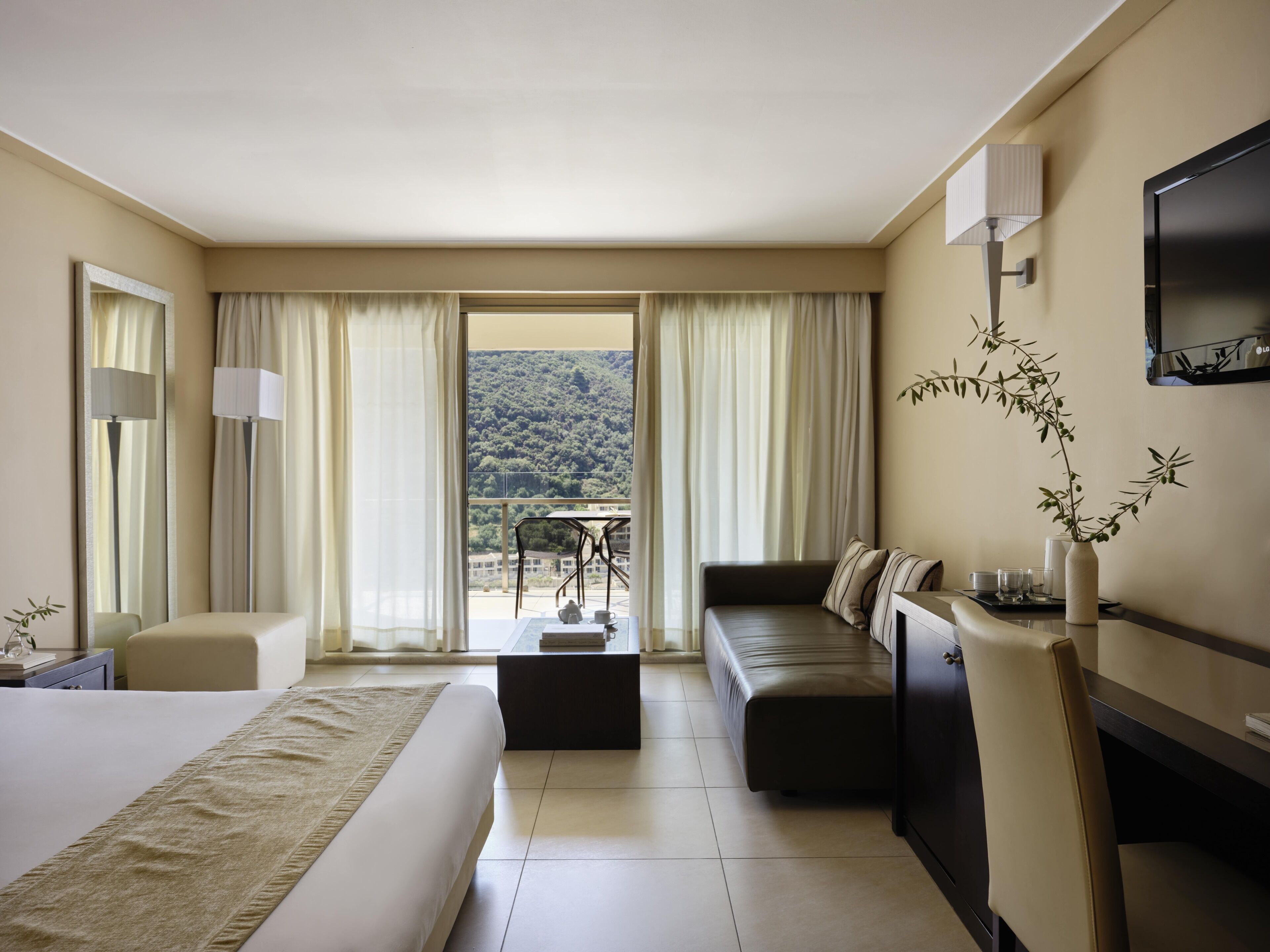 Een hotelkamer met een bed, een sofa, een bureau, een televisie en uitzicht op een bergachtig landschap.