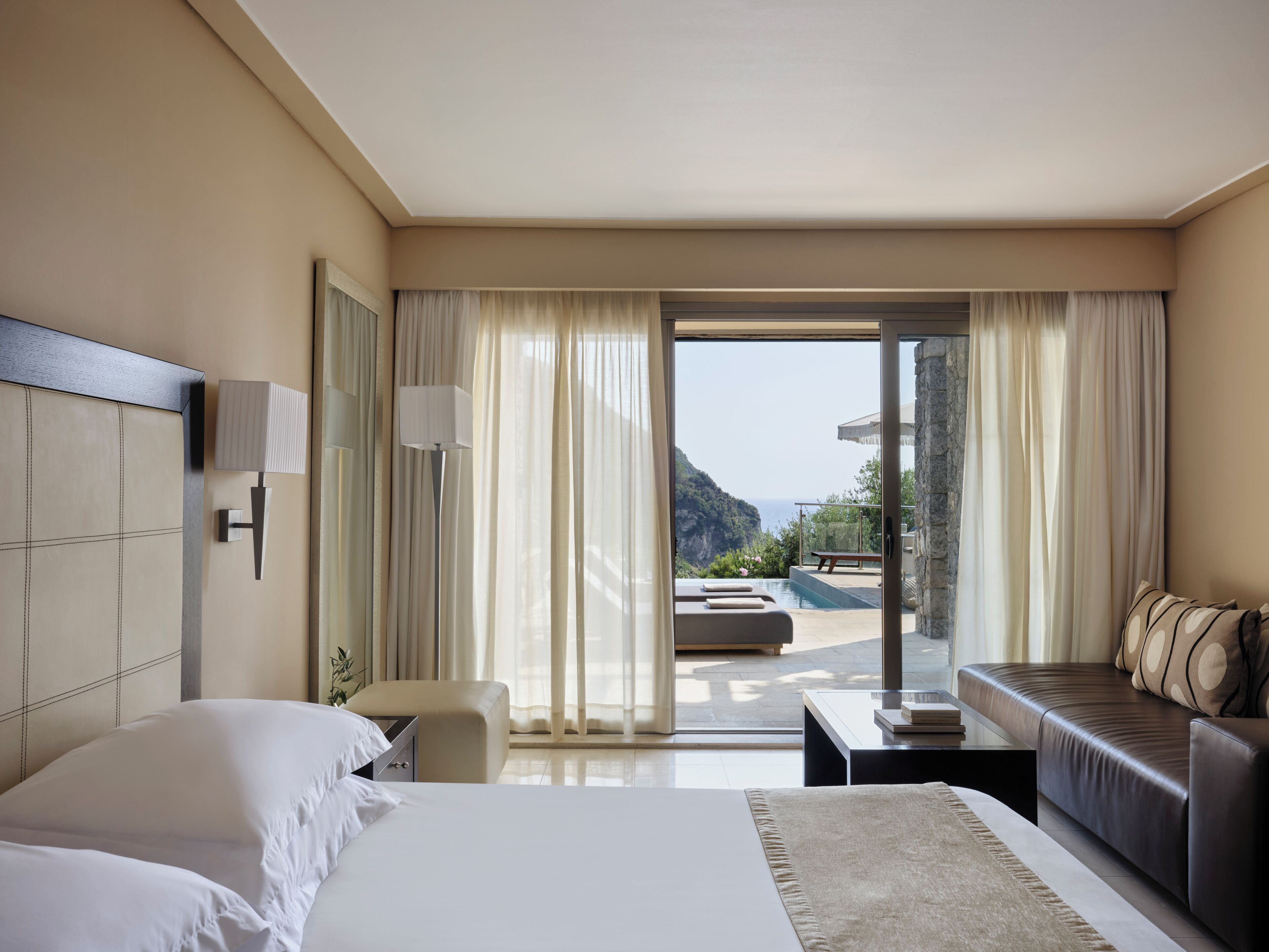 Een hotelkamer met een bed, een slaapbank, een tafeltje en uitzicht op de zee door een glazen schuifdeur.
