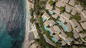 An aerial view of a coastal hotel with multiple swimming pools, a beach, and a road running alongside. - Atlantica Grand Mediterraneo Resort - Adults Only (Corfu)