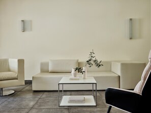 A minimalist living room with a white sofa, a black armchair, a glass coffee table with books, and a potted plant. - Atlantica Grand Mediterraneo Resort - Adults Only (Corfu)