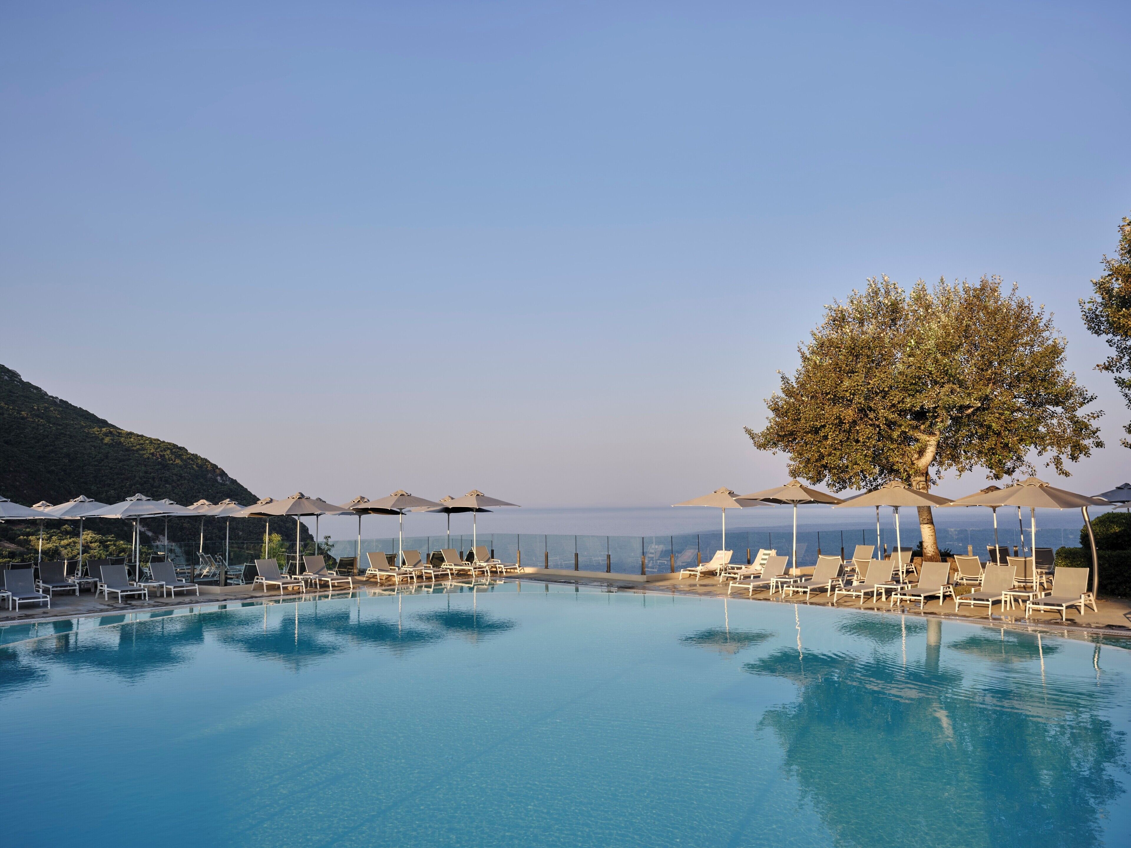 Una piscina con tumbonas y sombrillas, rodeada de un cielo despejado y vistas al mar.