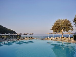 A pool with lounge chairs and umbrellas, surrounded by a clear sky and a view of the sea. - Atlantica Grand Mediterraneo Resort - Adults Only (Corfu)