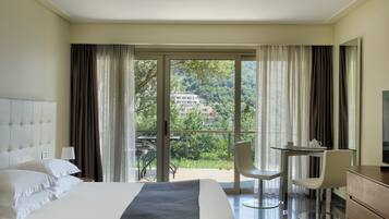 Habitación de hotel con cama, escritorio, dos sillas y un balcón con vistas a zonas verdes y edificios.