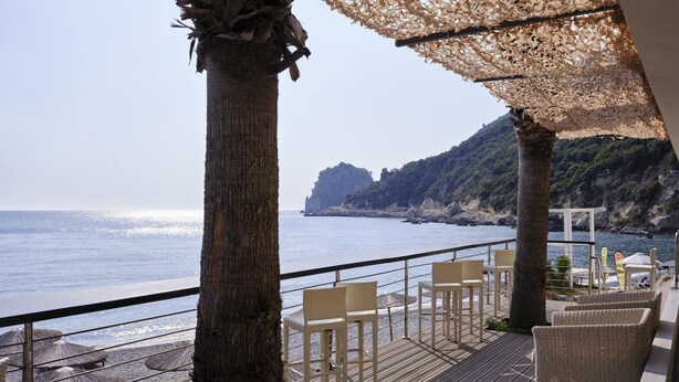 A deck with wicker chairs overlooking a beach and the sea. - Atlantica Grand Mediterraneo Resort - Adults Only (Corfu)