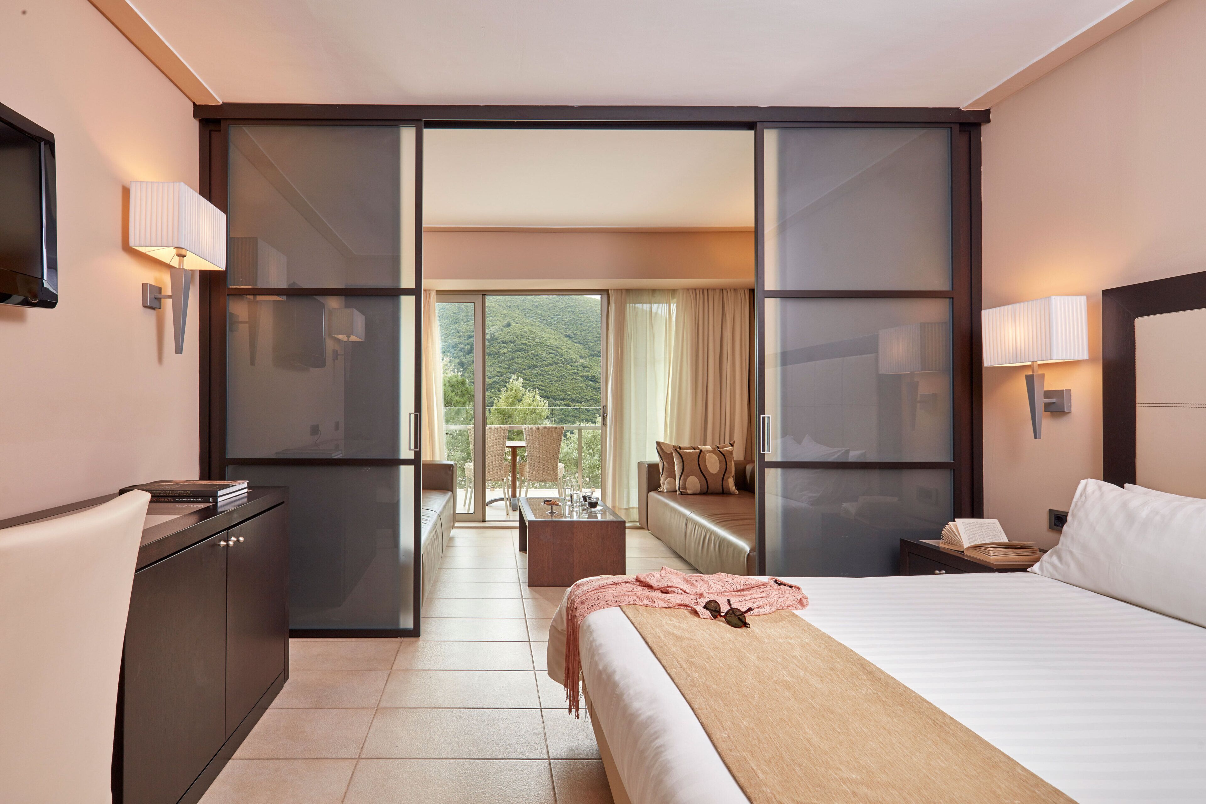 Een hotelkamer met een bed, een bureau, een stoel, een bank, een balkon met uitzicht en een televisie.