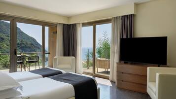 Une chambre d’hôtel avec un lit, une télévision, un balcon avec une table et des chaises, et une vue sur la mer.