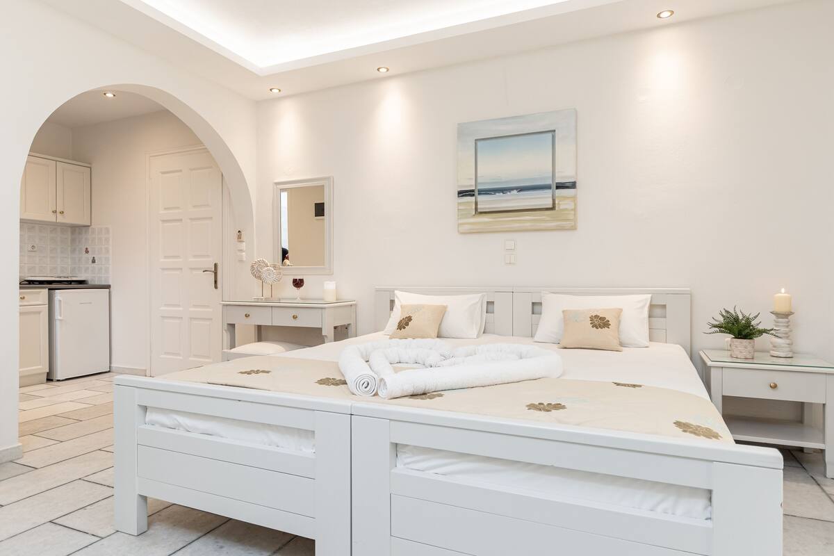 A modern bedroom with a large bed, a bedside table, a nightstand, and a view of the beach through a window.