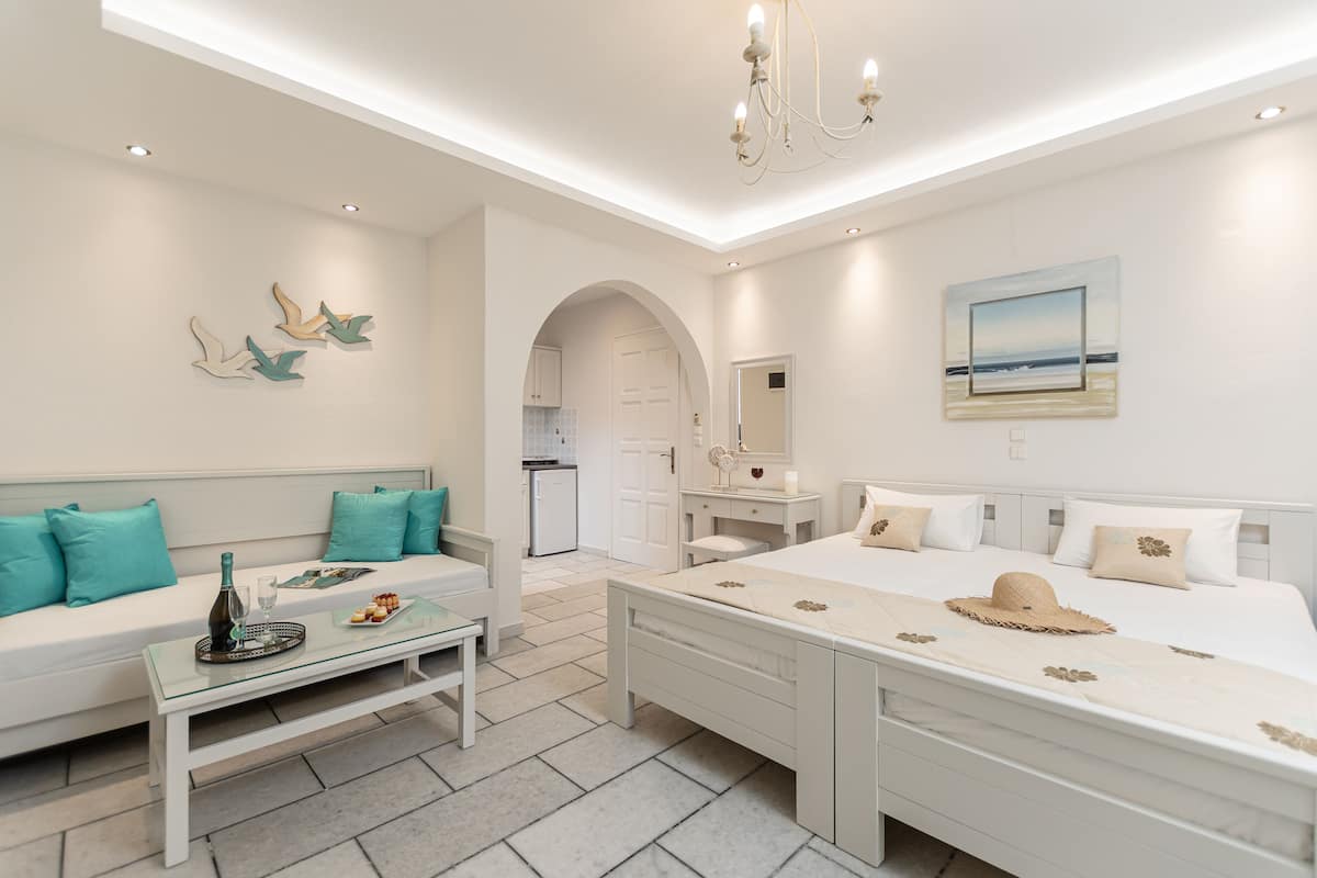 A modern bedroom with a large bed, a sofa, a small table, and a kitchen in the background.