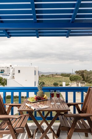 Una mesa de madera con una bandeja de frutas, dos copas de vino y un menú en un balcón con barandas azules.