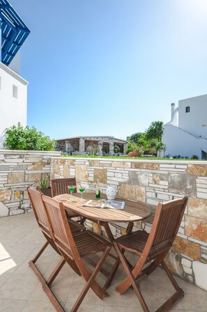 Un patio al aire libre con una mesa redonda de madera y cuatro sillas, un muro de piedra y vista a un edificio al fondo.