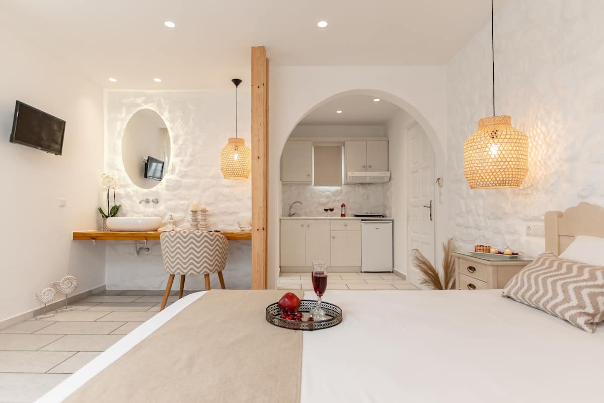 A modern hotel room with a bed, bedside table, and a small kitchen area.