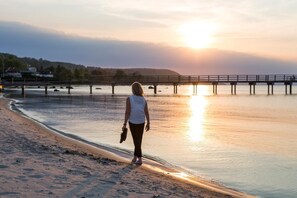 Henkilö kävelee rannalla, taustalla auringonlasku ja edessä veteen ulottuva laituri.