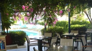 An outdoor seating area with tables and chairs, a pool, and a bookcase. - Costas & Chrysoula (Agios Vasileios)